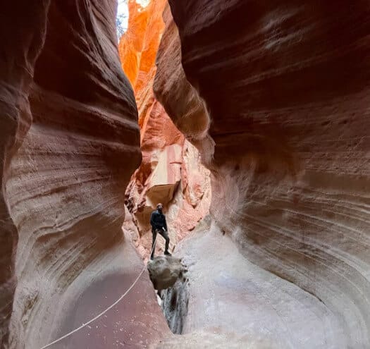 A person stands on a rock in a narrow, colorful canyon.